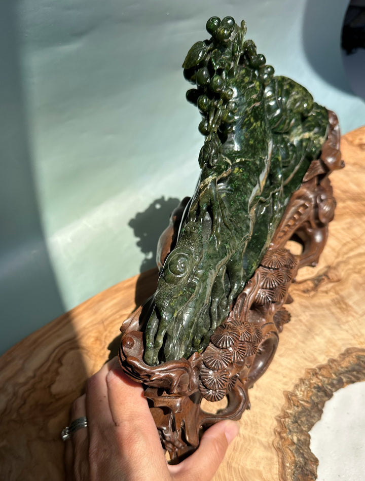 Angled side view of green jade Cassiar sculpture with grape vines and a floral carved wooden base