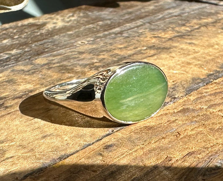 Green jade ring with oval cabochon displayed on a sunlit wooden surface