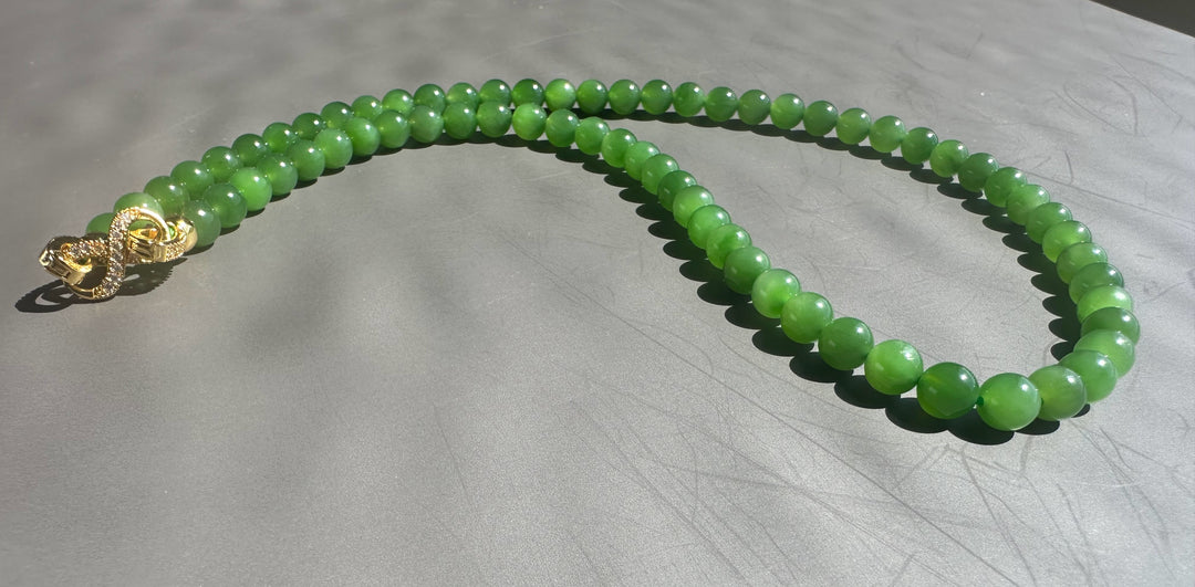 Green beaded necklace with a gold clasp on a light gray surface