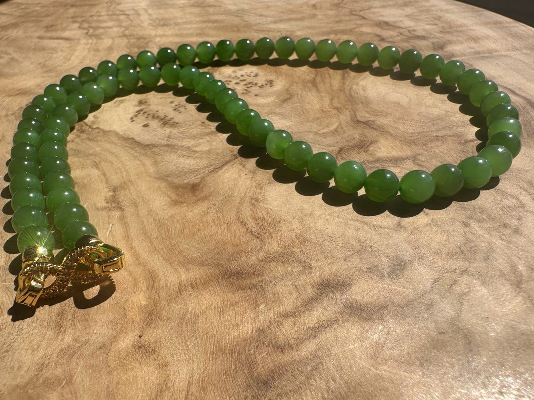 Green beaded necklace with a gold clasp on a wooden surface