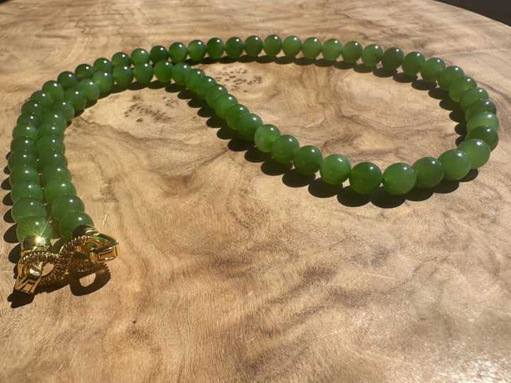 Green beaded necklace with a gold clasp on a wooden surface