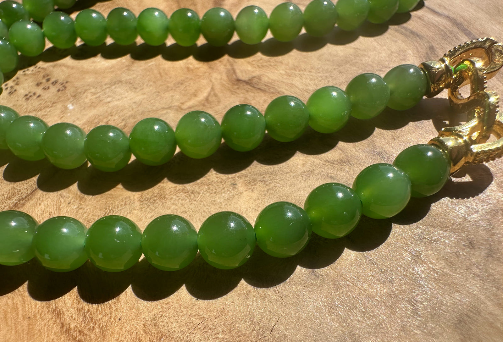 Green beaded necklace with a gold clasp on a wooden surface