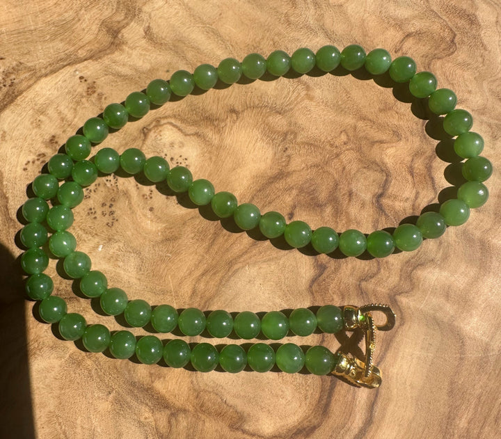 Green beaded necklace with a gold clasp on a wooden surface
