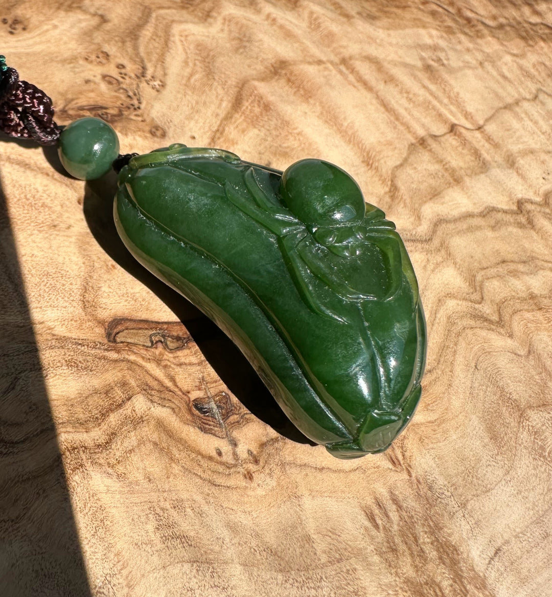Canadian jade spider and gourd pendant carved from deep green jade on a brown braided cord
