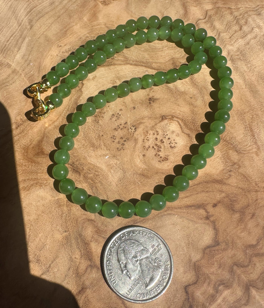 Green beaded necklace on a wooden surface with a coin for scale
