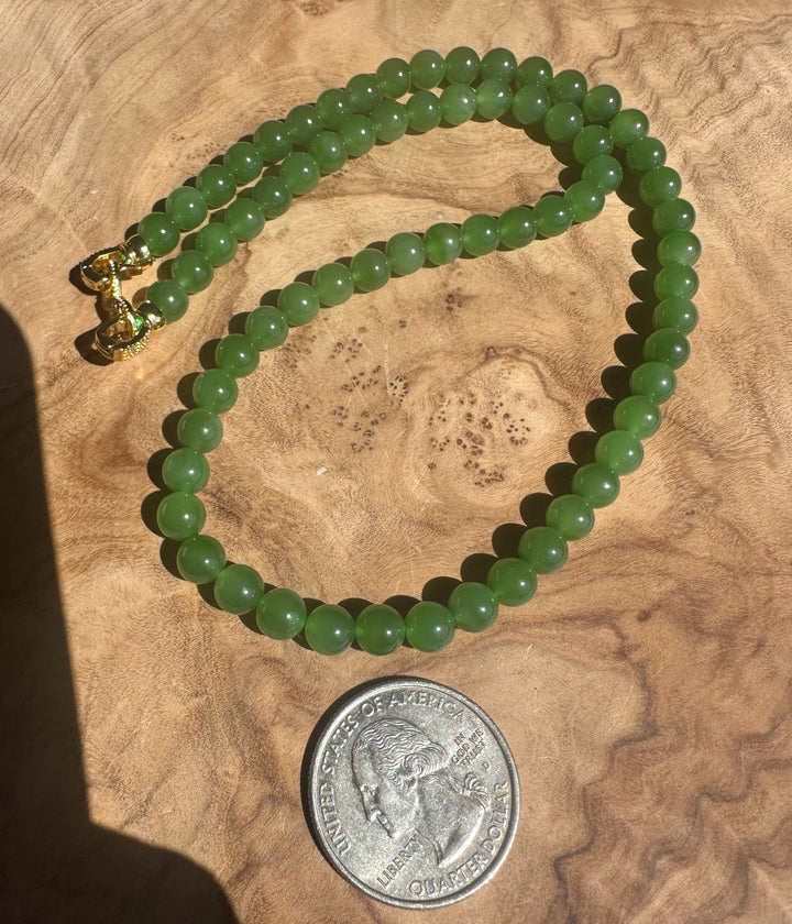 Green beaded necklace on a wooden surface with a coin for scale