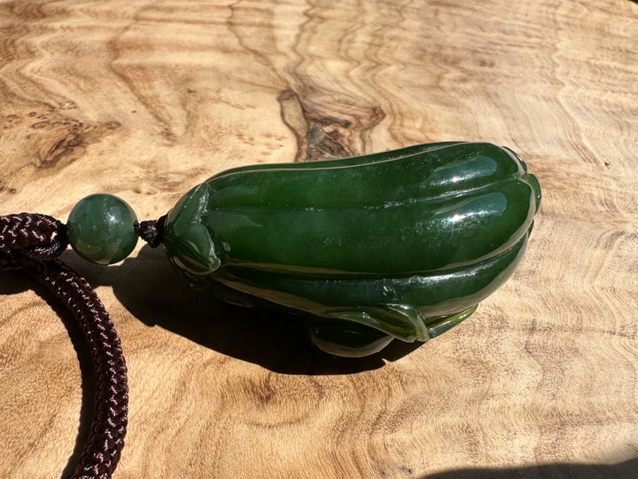 Round green jade bead above a carved spider and gourd pendant on a brown cord
