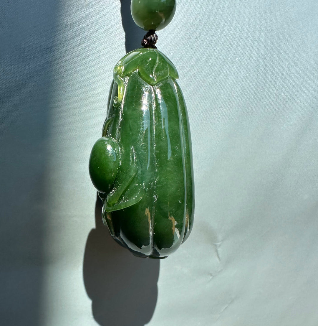 Close-up of jade gourd pendant showing vertical ridges and leaf detail on a brown cord