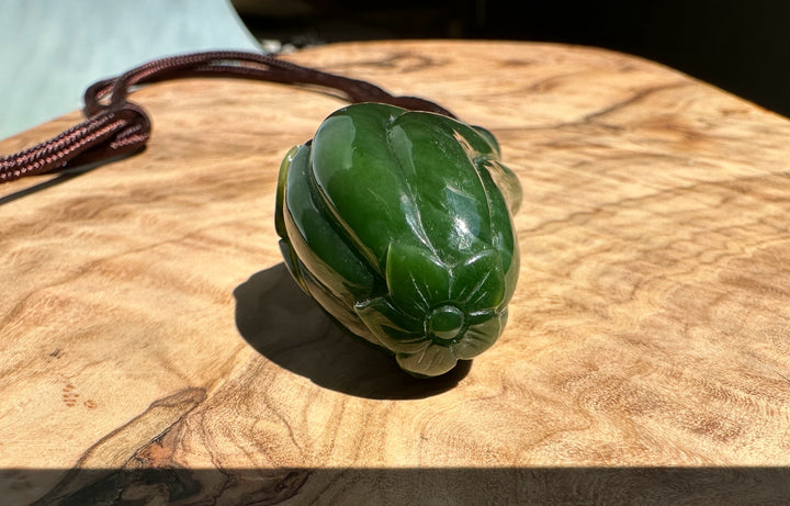 Green jade Spider and Gourd Pendant on a brown cord resting on a wooden surface.