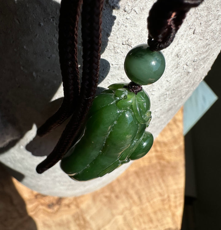 Side view of the jade spider and gourd pendant on a brown braided cord