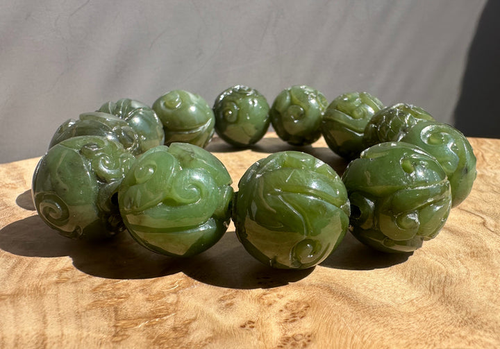 Green jade bracelet with intricate carvings on a wooden surface