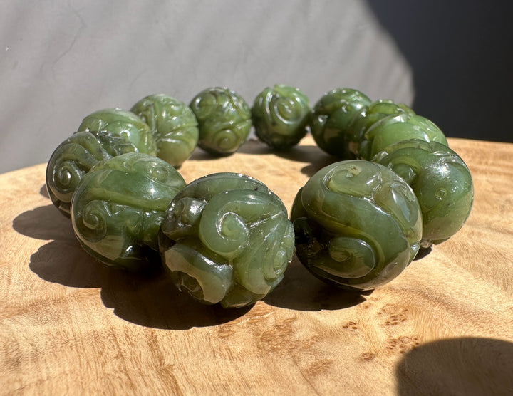Green jade bracelet with intricate carvings on a wooden surface