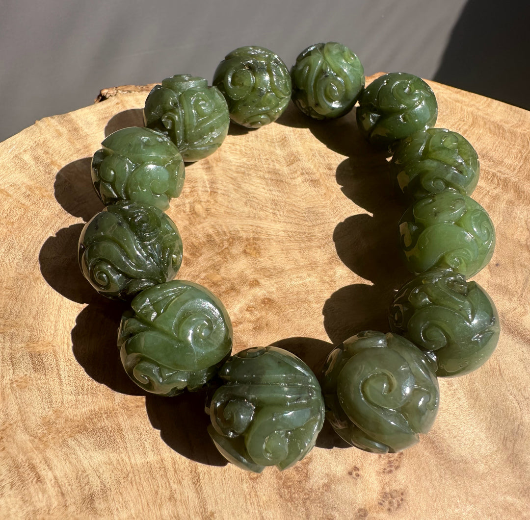 Green jade bracelet with intricate carvings on a wooden surface