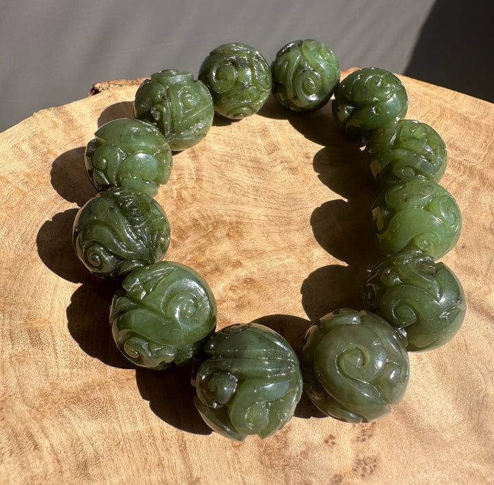 Green jade bracelet with intricate carvings on a wooden surface