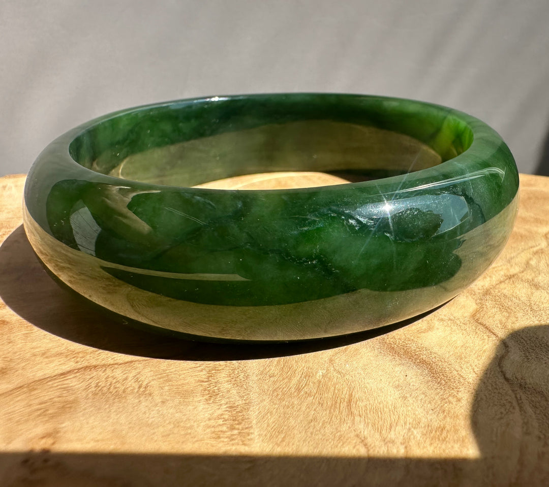 Green jade bangle on a wooden surface with a neutral background