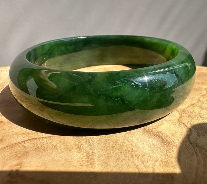 Green jade bangle on a wooden surface with a neutral background