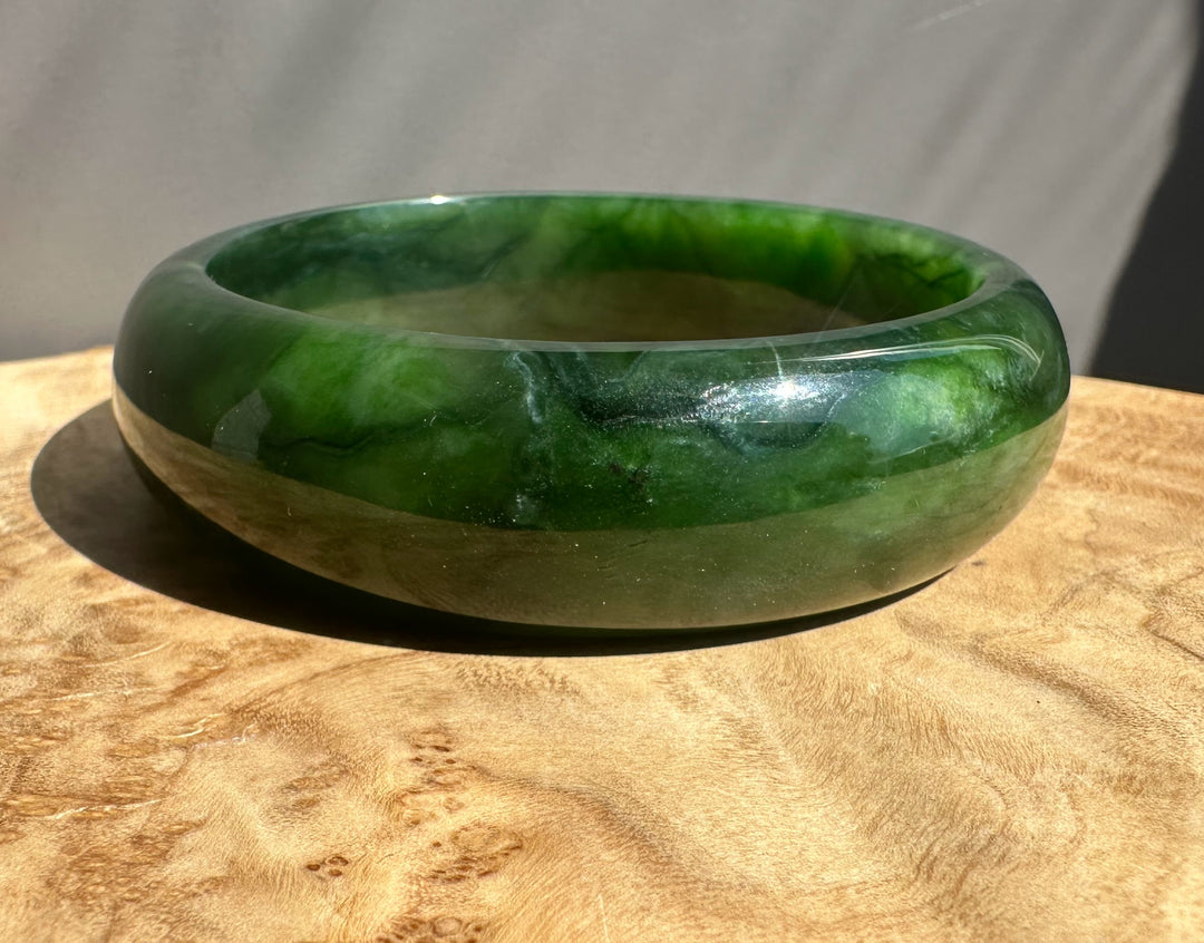 Green jade bangle on a wooden surface with a neutral background