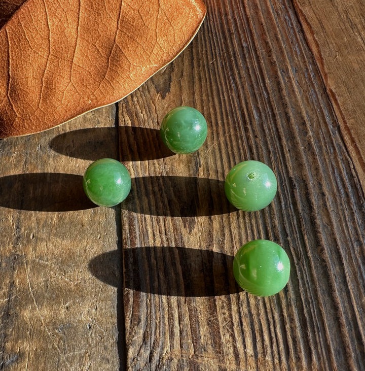 Group of four bright green jade beads on weathered wood near a dried leaf.