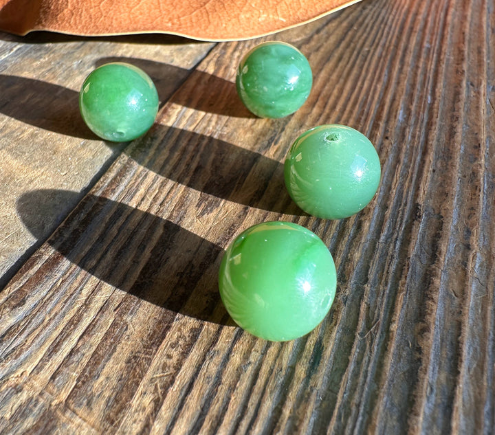 Four 14mm Siberian jade beads scattered on a rustic wooden surface.