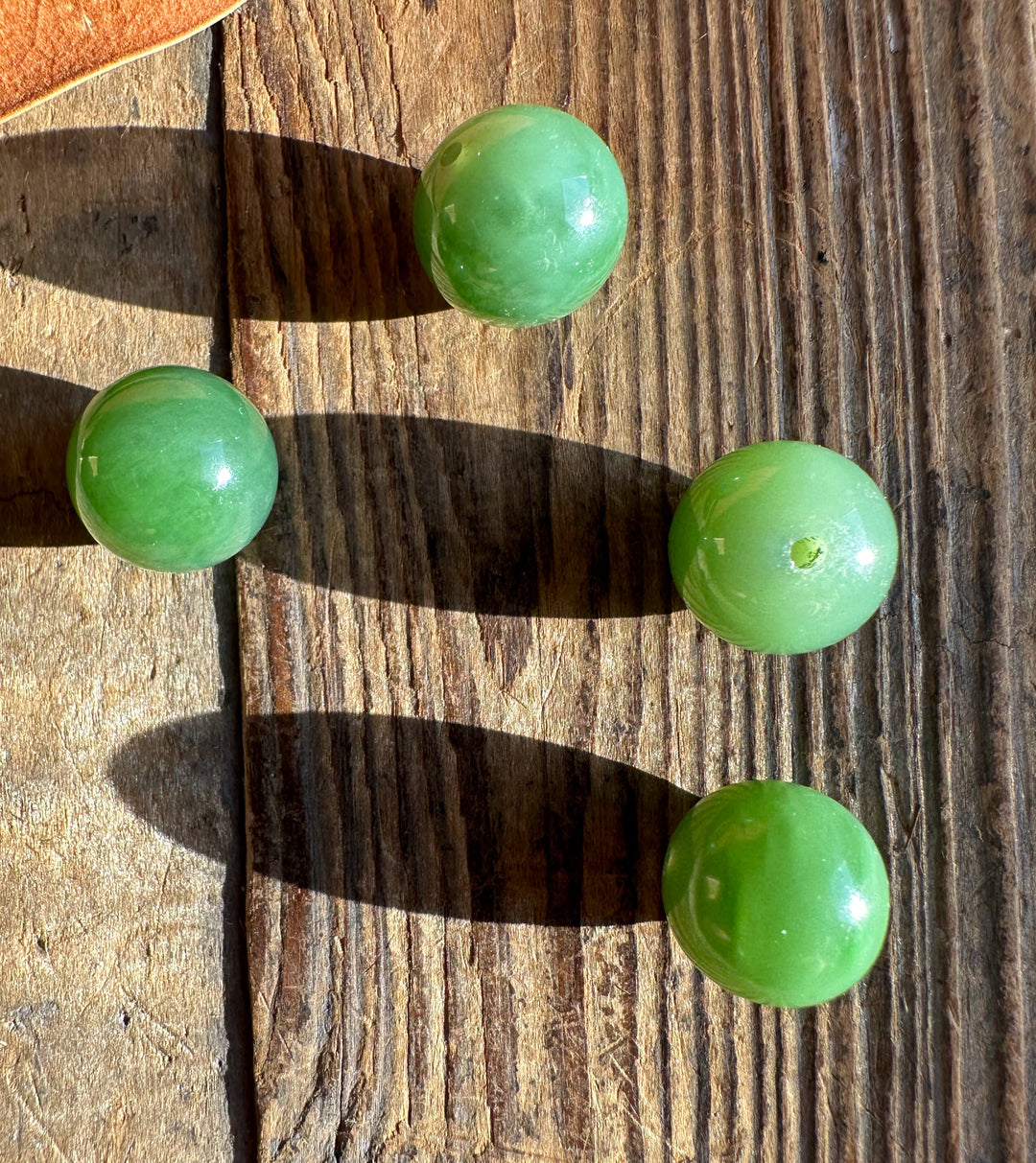 Four green 14mm jade beads resting on a weathered wooden surface in sunlight