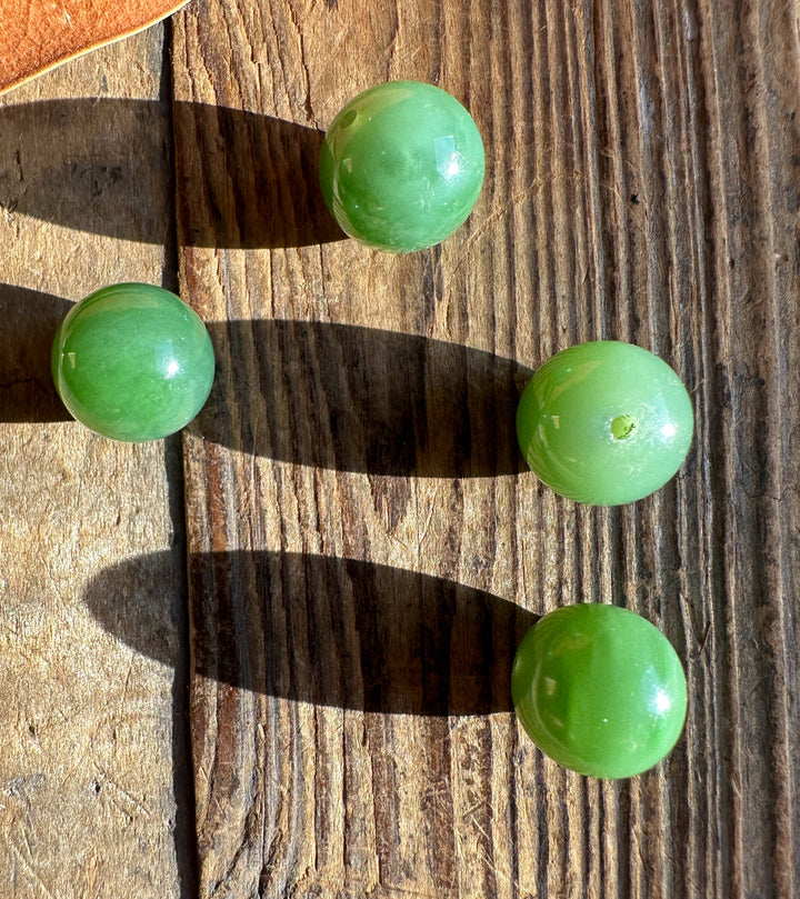 Four green 14mm jade beads resting on a weathered wooden surface in sunlight