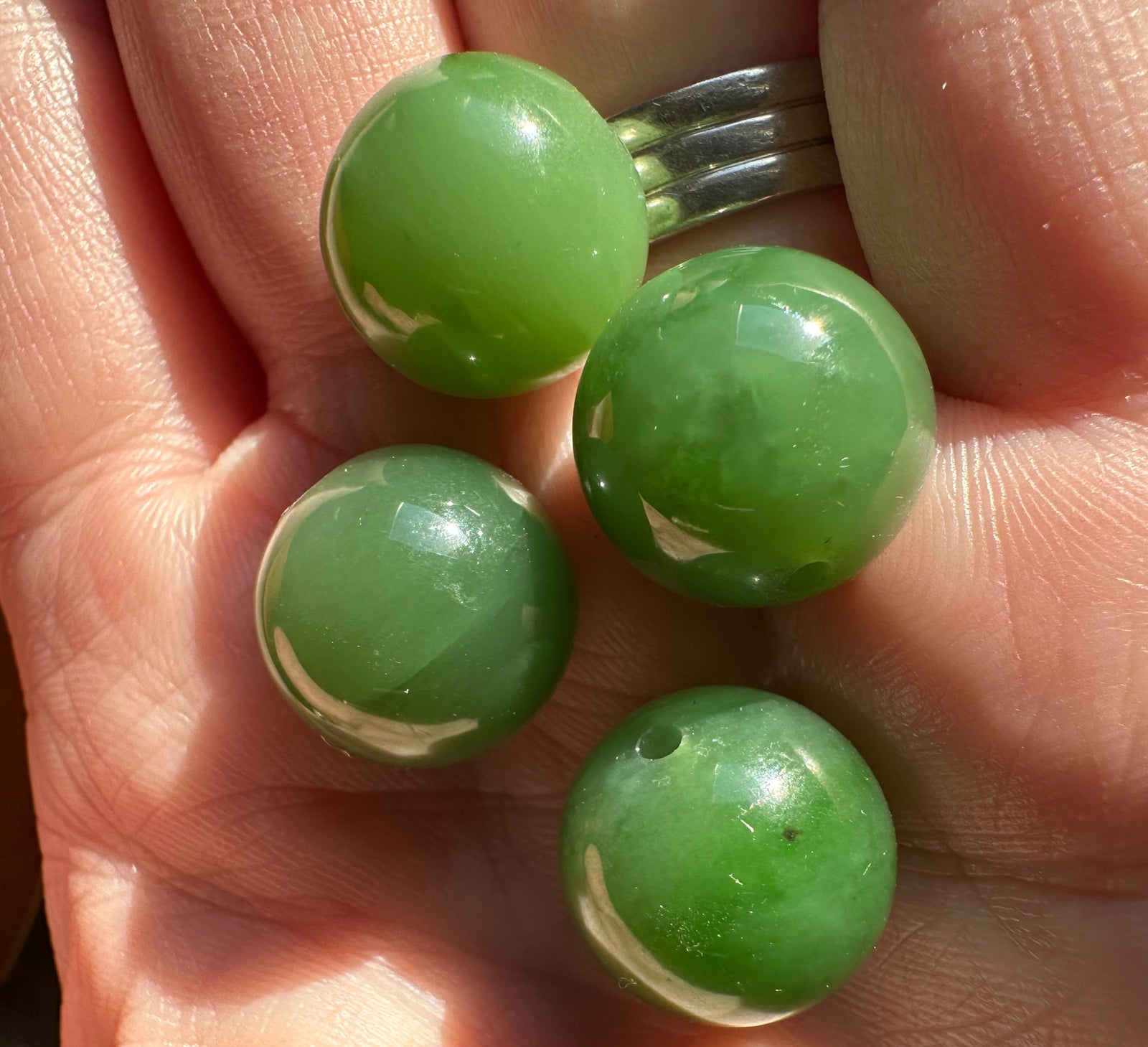 Four green 14mm polished Siberian jade beads held in a hand with a silver ring in the background