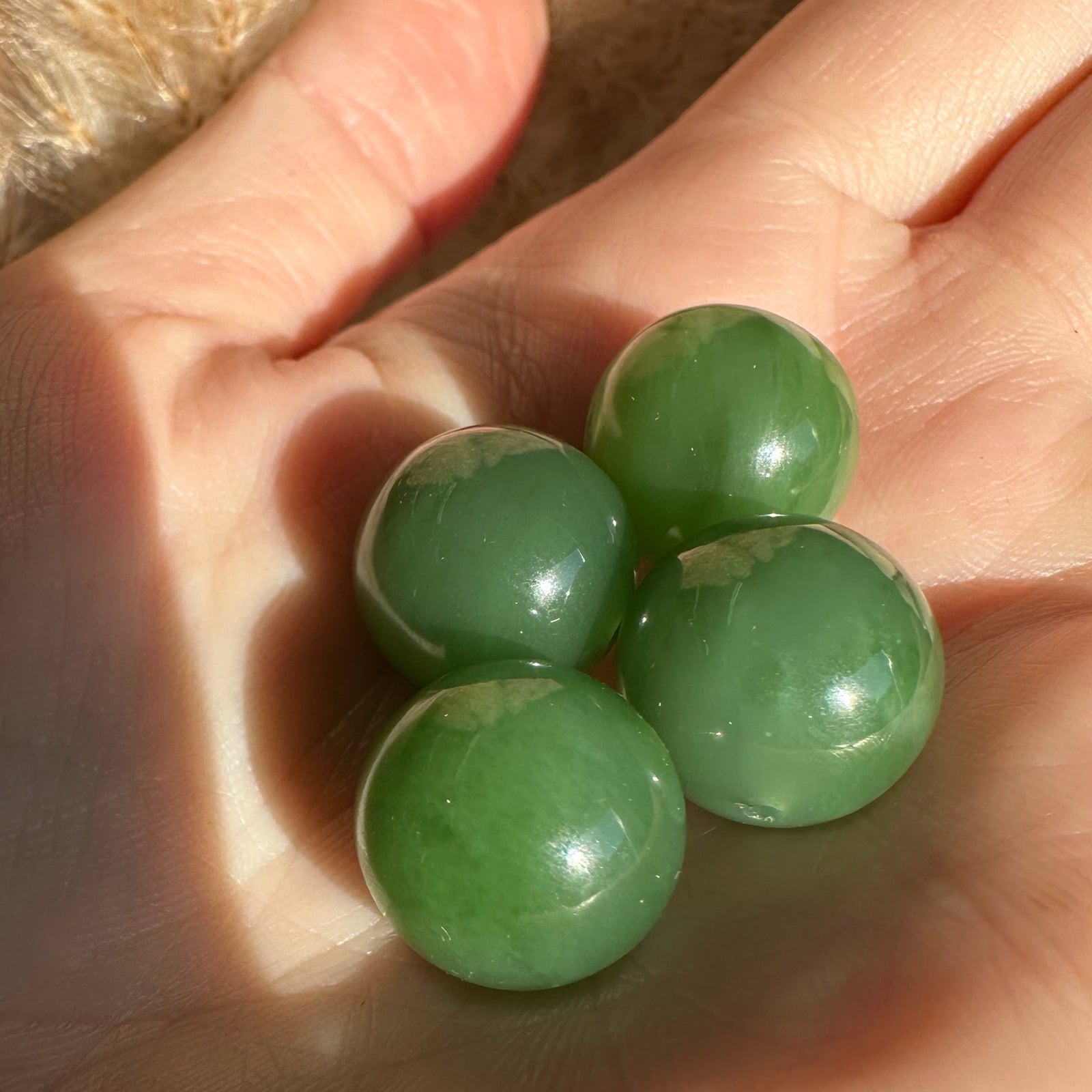 Four green 14mm polished Siberian jade beads held in a hand
