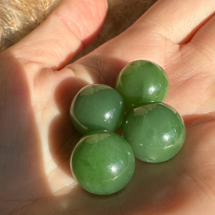 Four green 14mm polished Siberian jade beads held in a hand