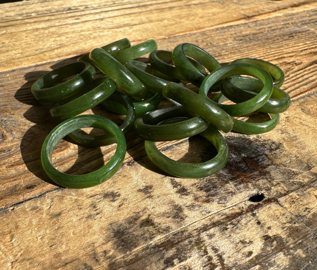 Group of green jade band rings scattered across a weathered wooden surface