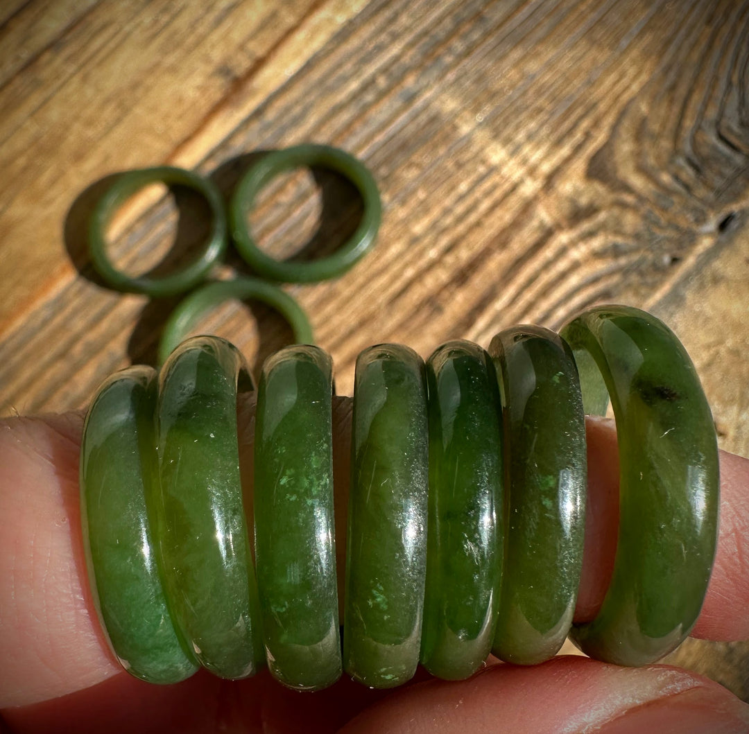 Close up of polished green jade bangles held on a finger with more bangles in the background