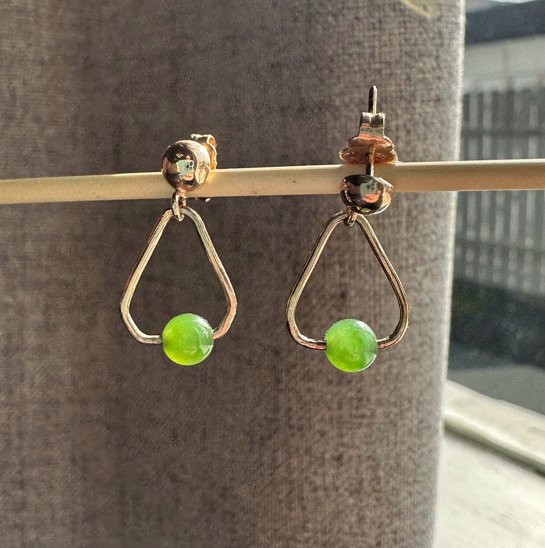 Two vintage jade earrings with gold triangular frames and green beads hanging from a rod