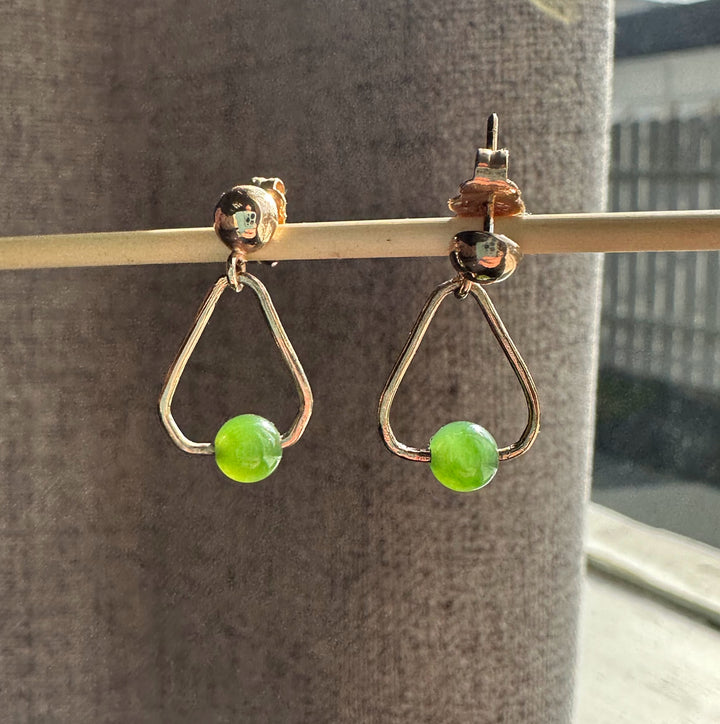 Two vintage jade earrings with gold triangular frames and green beads hanging from a rod