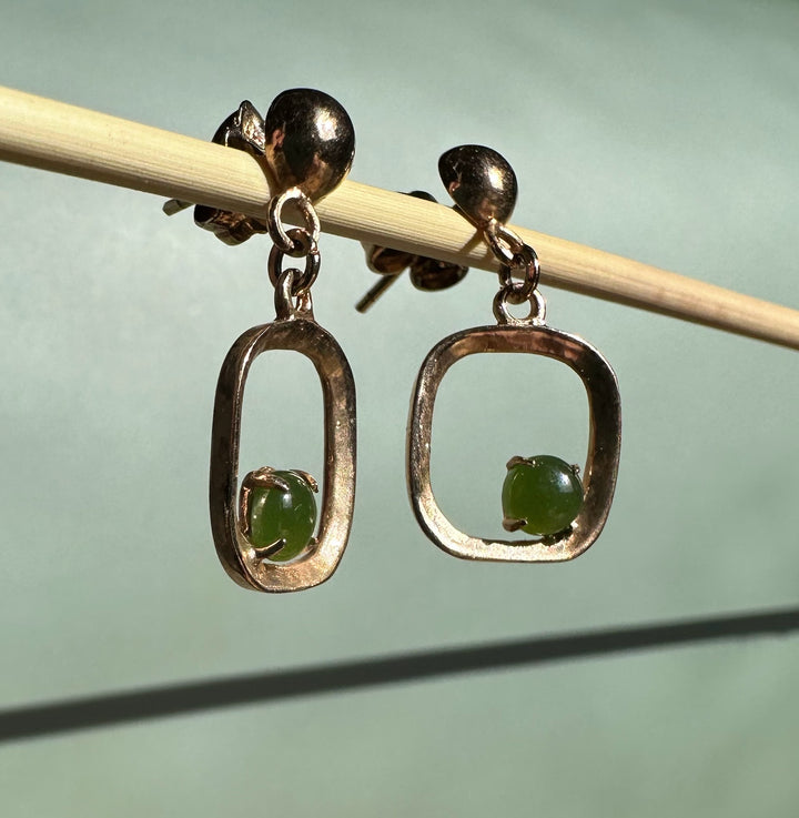 Pair of gold-tone drop earrings with open rectangular frames and green stones hung on a wooden rod