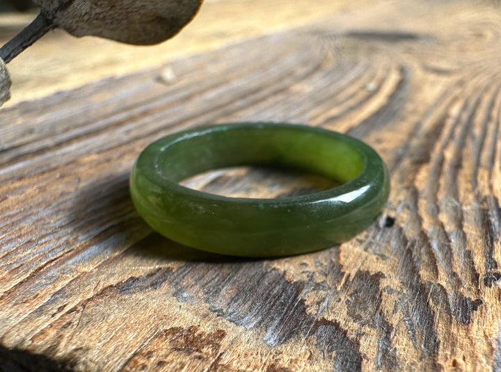 Close up of a single green jade band ring resting on a wooden surface