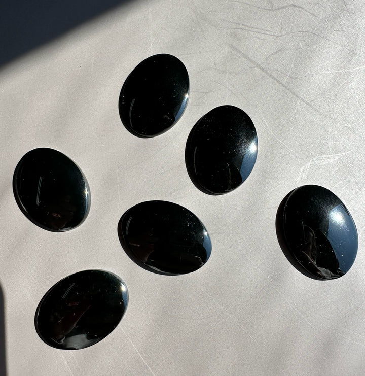Polished jade oval cabochons in dark green to blue tones spread across a light textured surface.