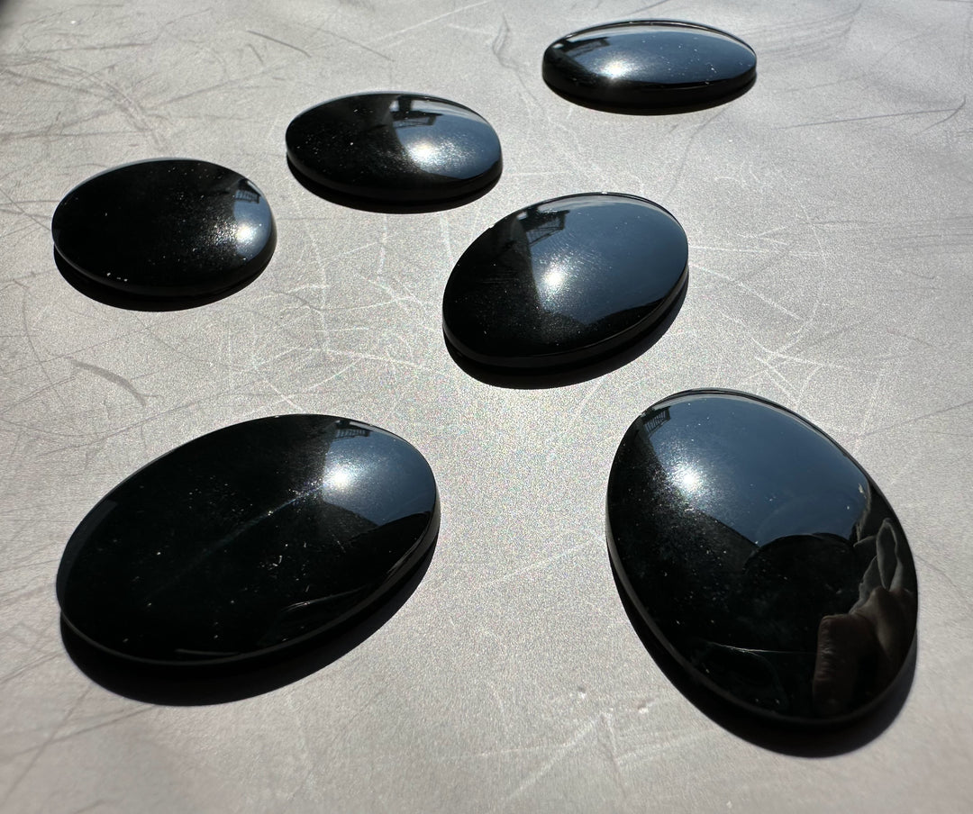 Glossy jade oval cabochons in deep green to near black tones arranged on a pale background.