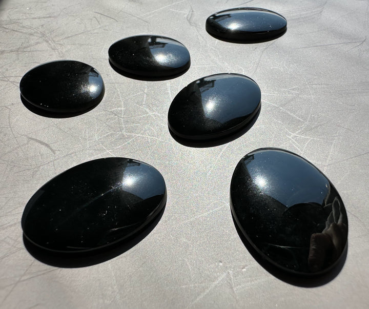 Glossy jade oval cabochons in deep green to near black tones arranged on a pale background.