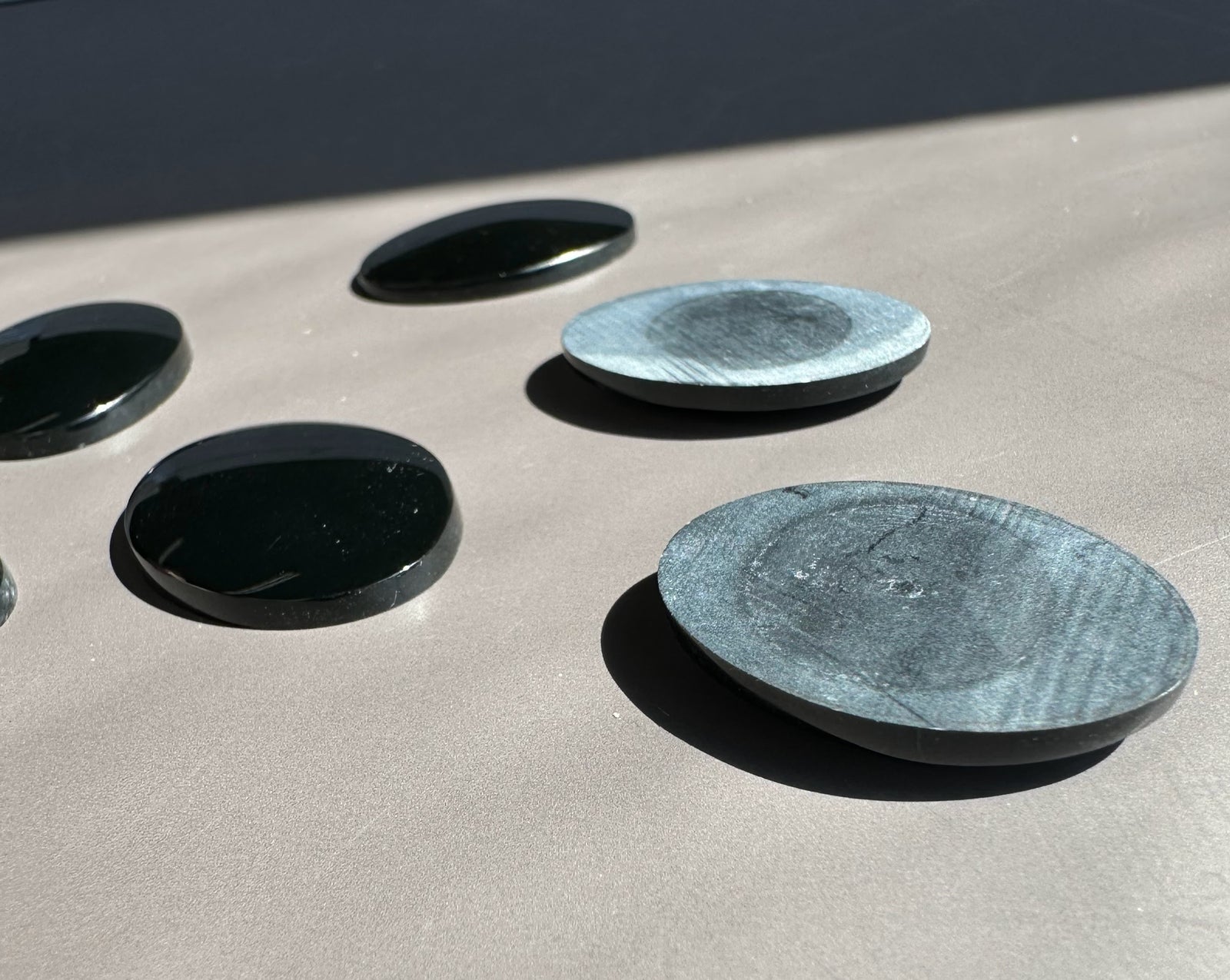 Wyoming Edwards Jade oval cabochons in dark green with a blue green piece among them on a light surface.