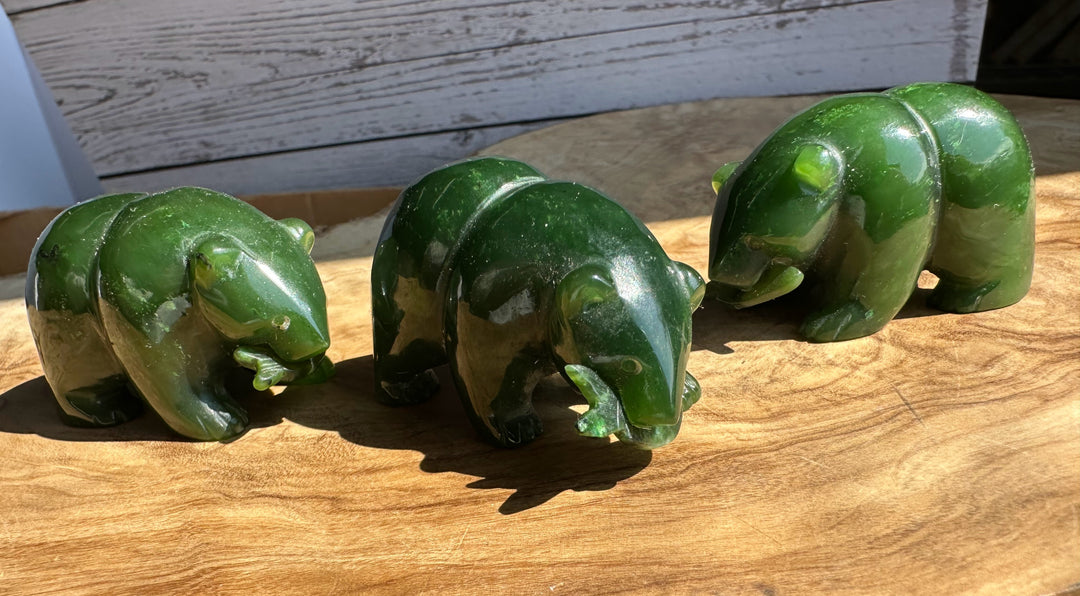Three glossy green jade bear figurines lined up on a wooden surface