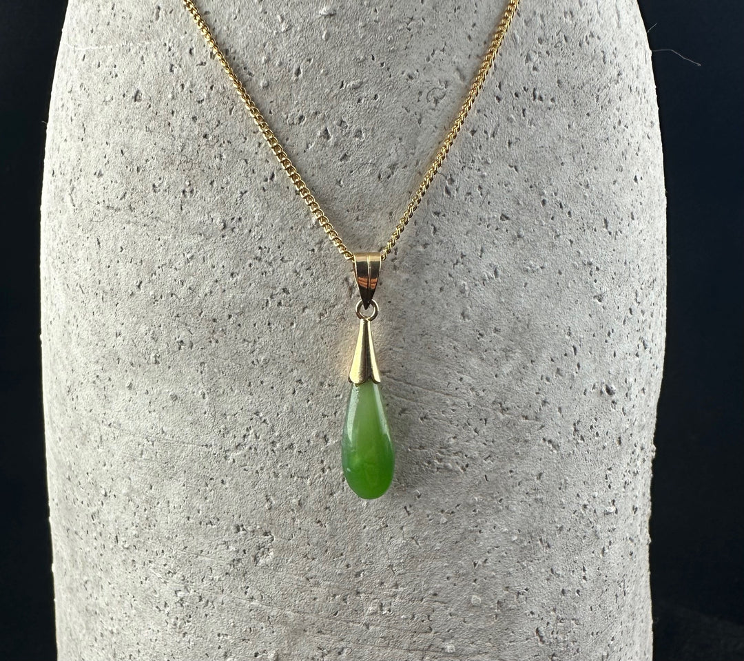 Vintage Teardrop Pendant in green jade on a gold chain displayed on a textured gray stand.