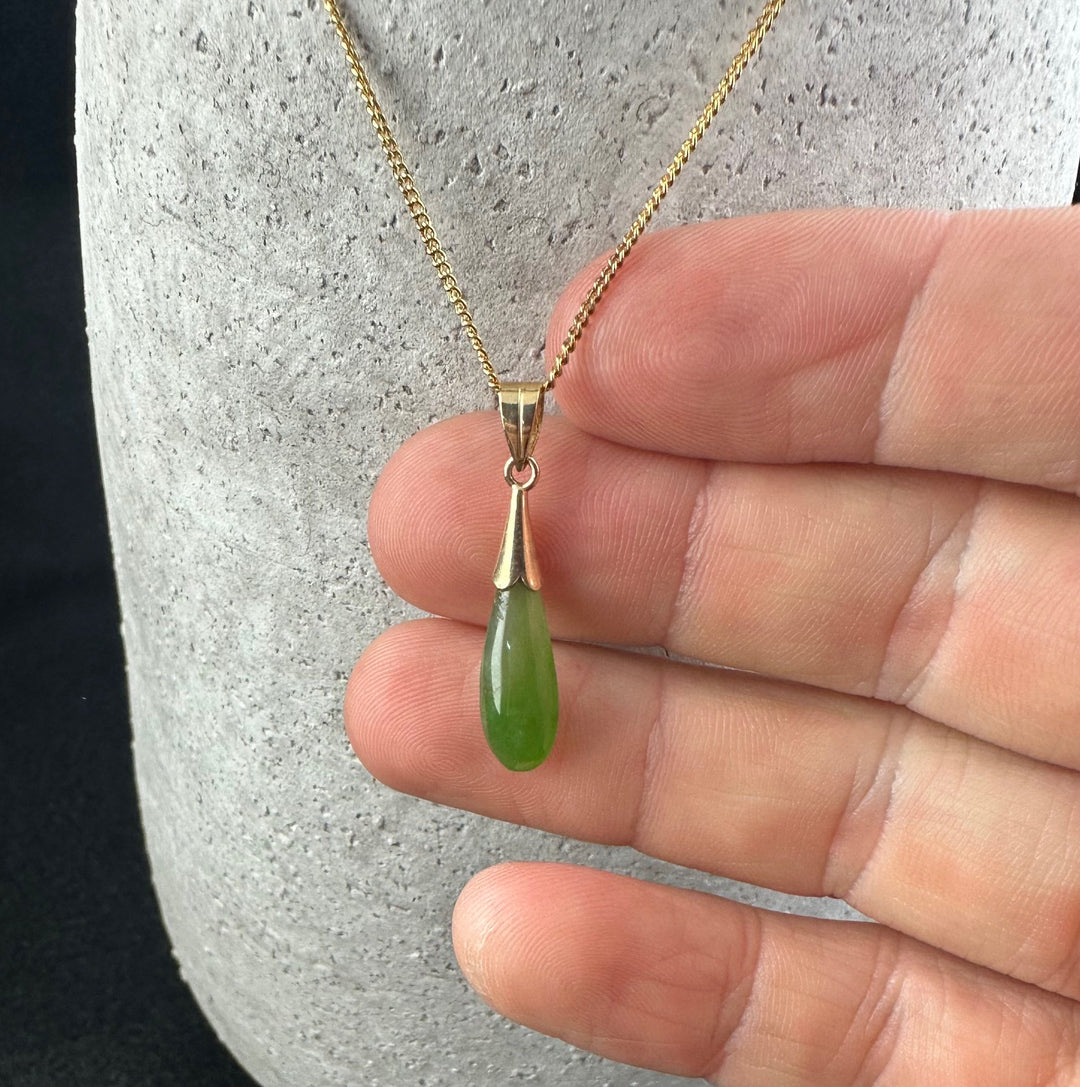 Close up of the vintage teardrop pendant with gold bail and green jade teardrop held by fingers.