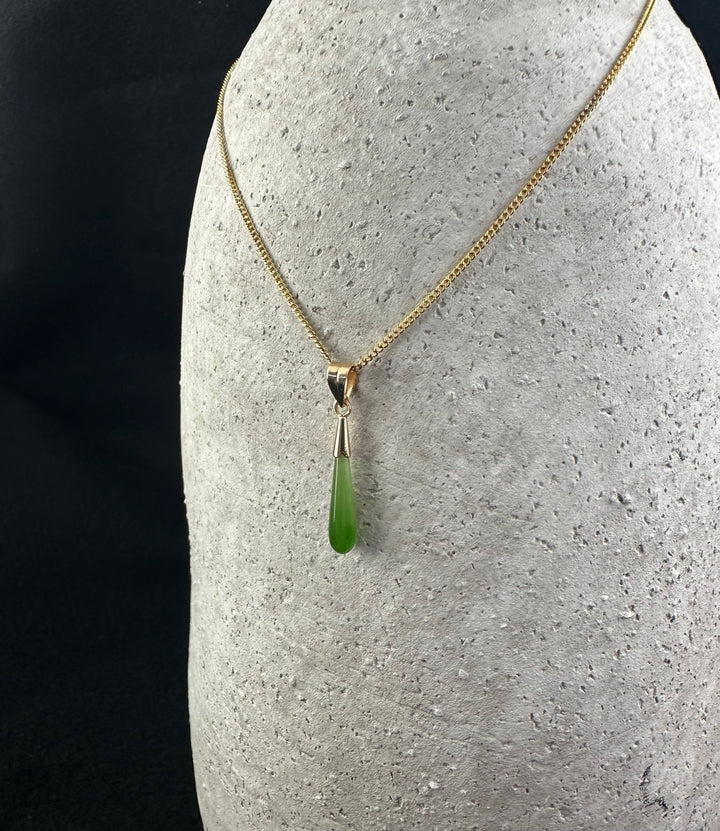 Gold chain necklace with a slender green teardrop pendant displayed on a stone bust