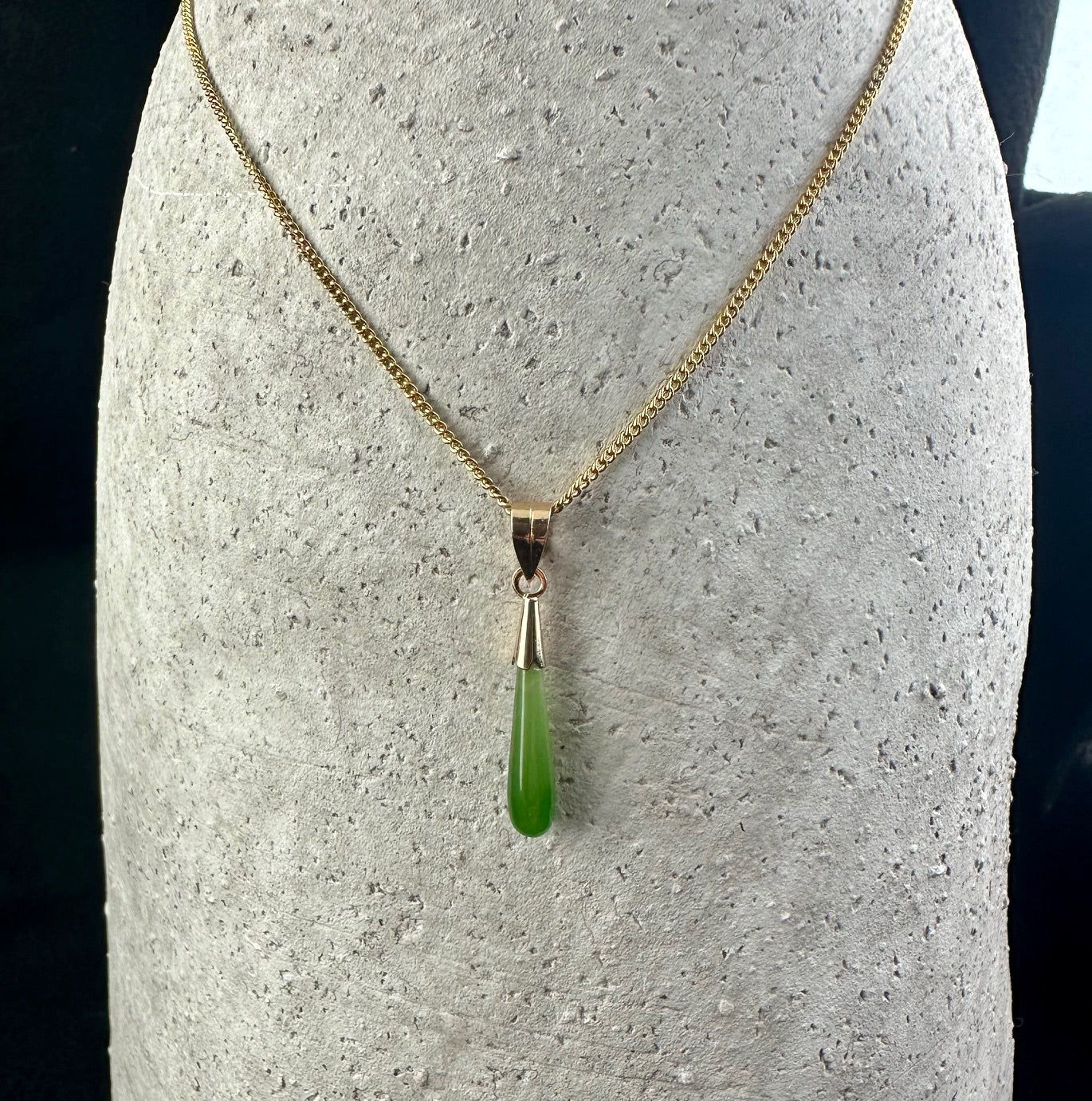 Vintage teardrop pendant in green jade hanging from a gold chain on a display bust