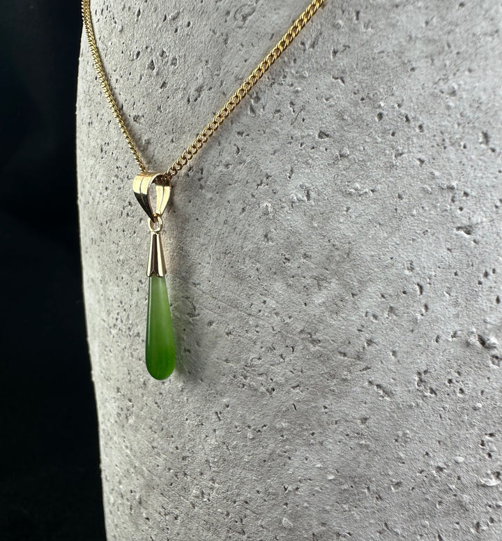 Close-up of gold teardrop pendant with a green gemstone drop on a gold chain