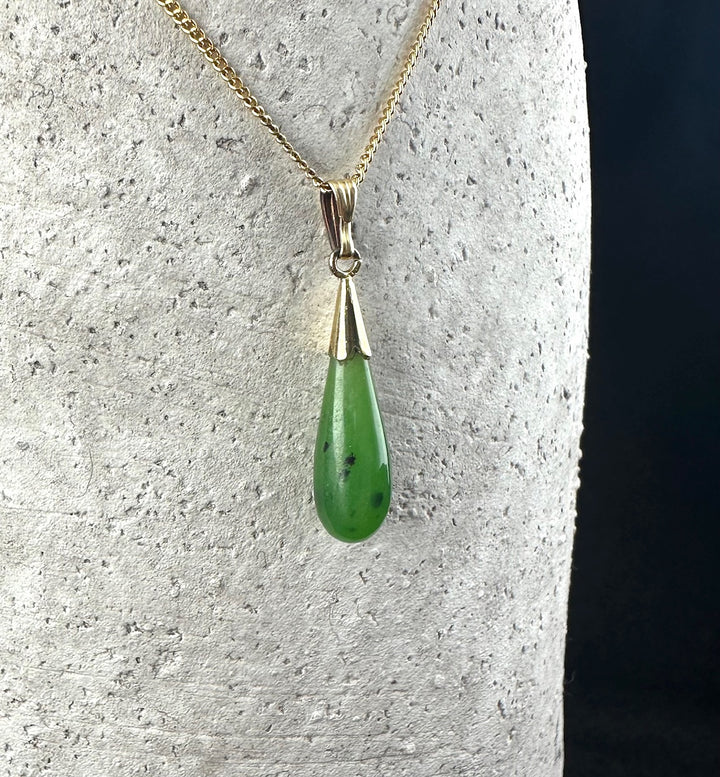 Vintage teardrop pendant with green gemstone on a gold chain against a textured background