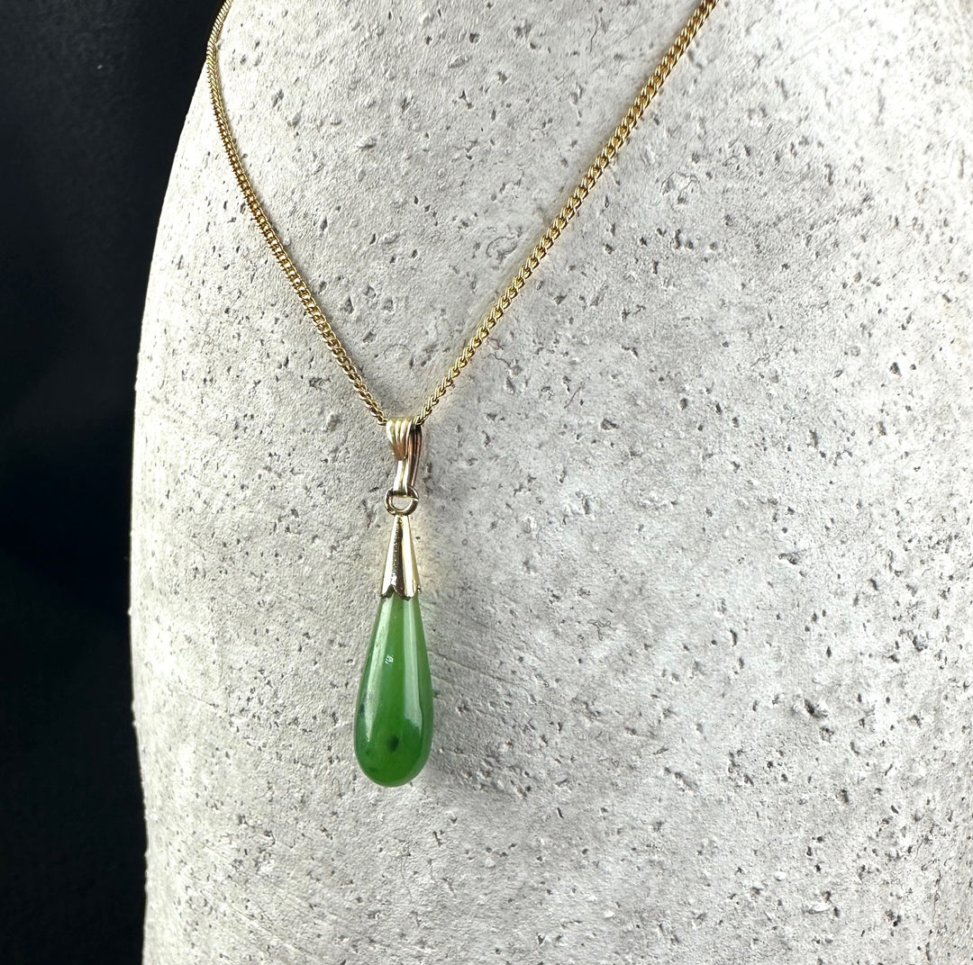 Gold chain necklace with a green teardrop pendant hanging from a decorative bail
