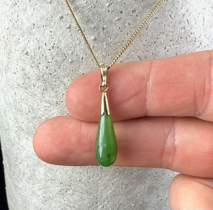 Green jade teardrop pendant on a gold chain held by fingers