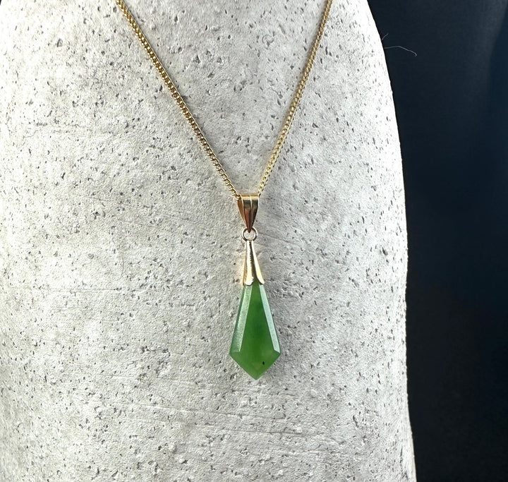 Gold chain necklace holding a green gemstone drop pendant against a textured background
