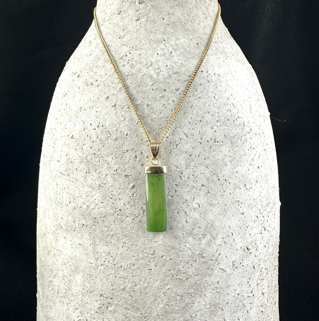Vintage rectangle drop pendant in green jade on a gold chain displayed on a bust stand