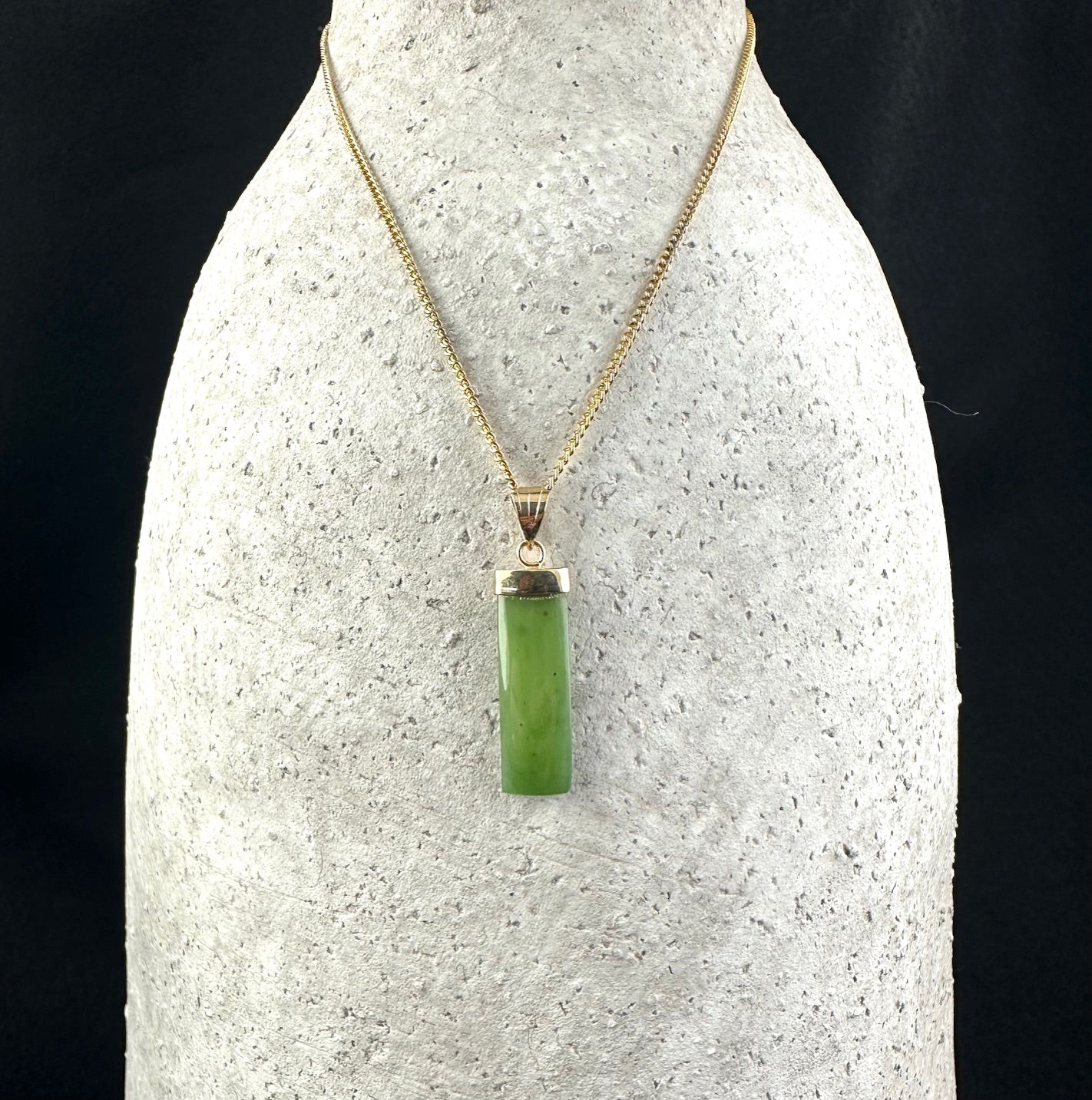 Vintage rectangle drop pendant in green jade on a gold chain displayed on a bust stand